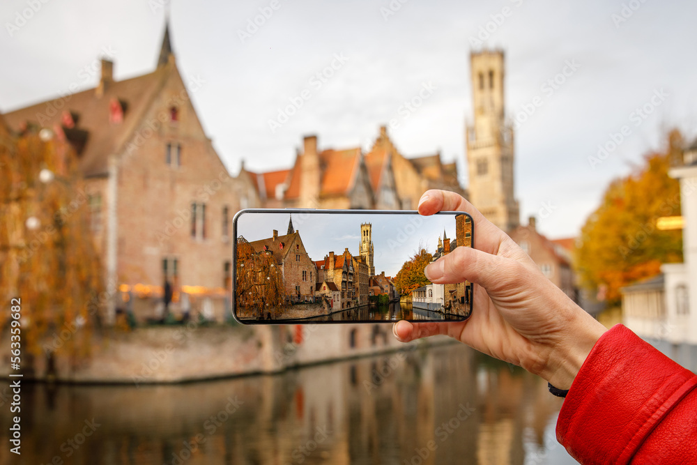 Fototapeta premium Traveling old Europe. Taking the picture of Brugge iconic view via smartphone.