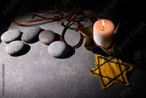 Holocaust memory day. Barbed wire, stones, yellow star and burning candle on black background photo