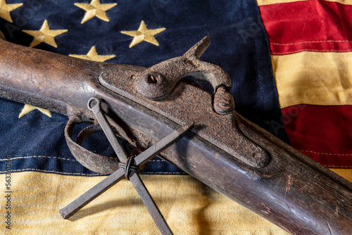 old rusted musket gun and metal cross on tea stained American flag