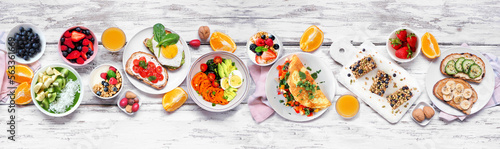 Healthy breakfast food table scene. Top down view over a white wood banner background. Omelette  nutritious bowl  toasts  granola bars  smoothie bowl  yogurts and fruits.