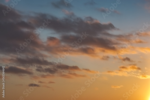 The minimalist warm sky at sunset in the evening with chaotic clouds, abstraction for the background, the clouds are highlighted by the sunset orange sun