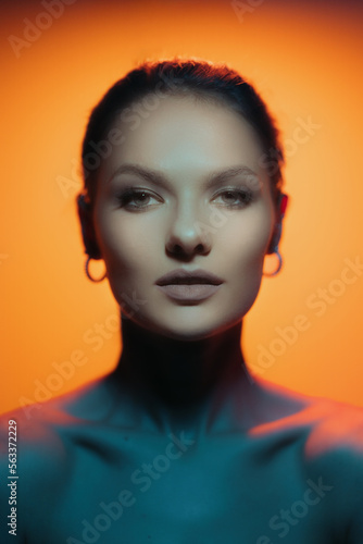 Fashion woman profile portrait on orange gradient background with soft blue light play on skin. Model looking at camera. Lights play.