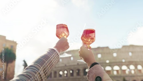 Female travellers in stylish clothes enjoying panoramic view of ancient Colosseum drinking refreshing cocktail in glass, friends enjoying vacation in the downtown of Rome cheering with cocktail drinks
