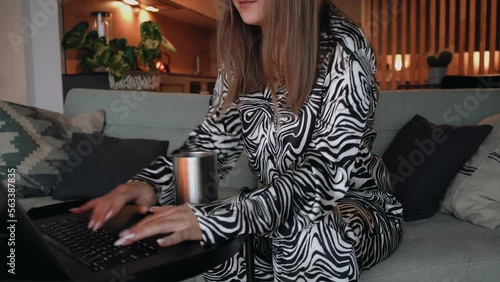 A girl in zebra pajamas jumps over the sofa to the computer and quickly writes a message. Morning bustle, deadline, work from home.