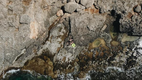 Top view drone rising from young couple in love on vacation lies on the seashore, top view. Waves wash over the rocky shore with azure blue water. Relax and vacation concept. Wild beach without people
