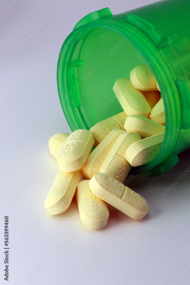 Green Prescription bottle of NSAID naproxen tablets spilling onto grey