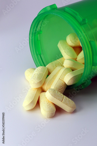 Green Prescription bottle of NSAID naproxen tablets spilling onto grey table