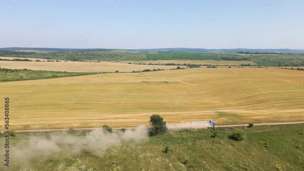 Aerial view of lorry cargo truck driving on dirt road between agricultural wheat fields. Transportation of grain after being harvested by combine harvester during harvesting season Aerial view of lorry cargo truck driving on dirt road between agricultural wheat fields. Transportation of grain after being harvested by combine harvester during harvesting season