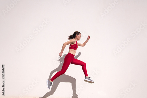 Sporty female running and jumping outdoors against a white wall.