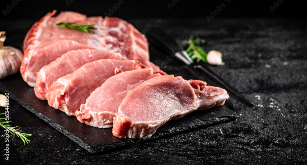 Chopped raw pork on a stone board with rosemary and garlic.