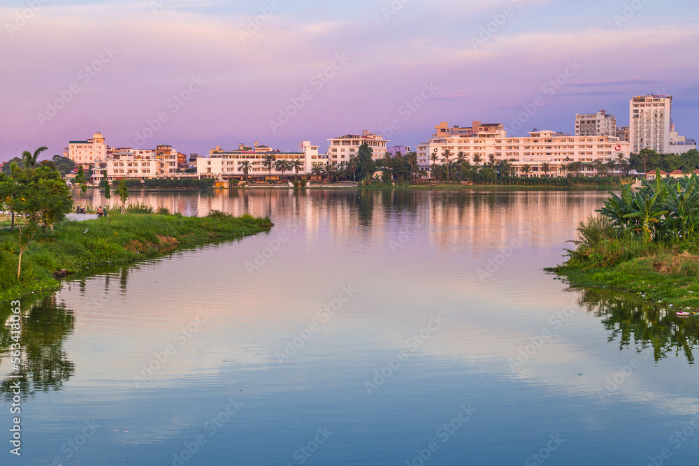 Buildings on a riverbank and a pink twilight sky reflected in the still water at Hue in Vietnam