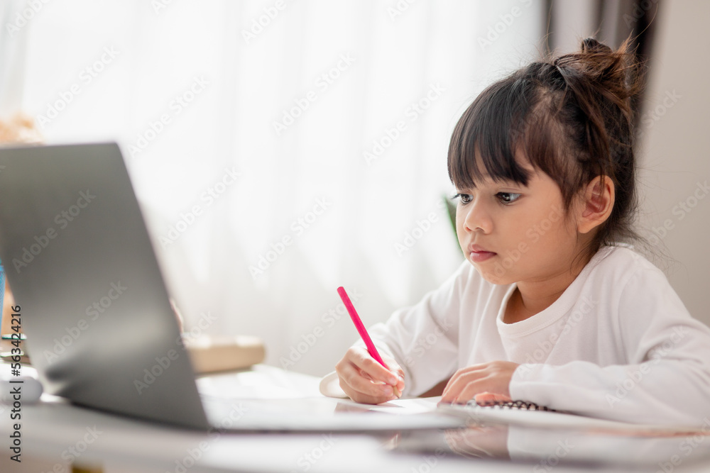 Asian schoolgirl doing her homework with laptop at home. Children use gadgets to study. Education and distance learning for kids. Homeschooling during quarantine. Stay at home