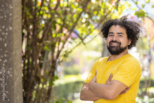 portrait of a Mexican man smiling with curly hair and beard arms crossed copy space