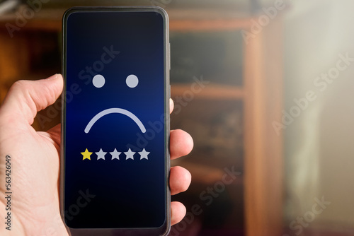 Fotografie Closeup of male hand holding mobile phone with sad face and one star rating