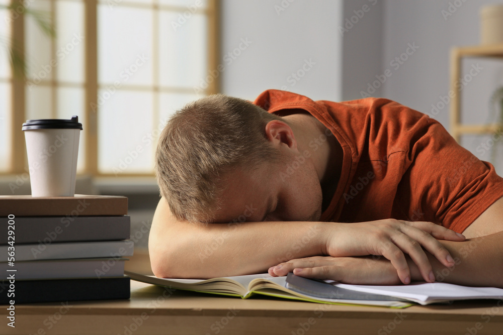 Obraz premium Tired man sleeping near books at wooden table indoors