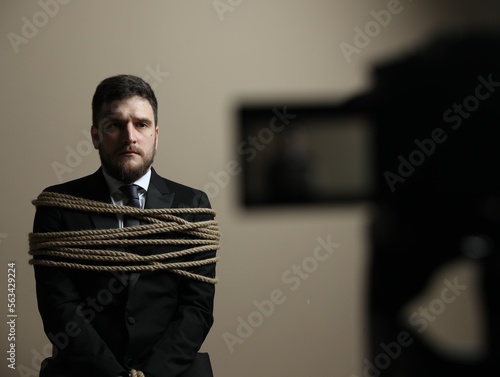 Photos Man tied up and taken hostage near camera on grey background, selective focus