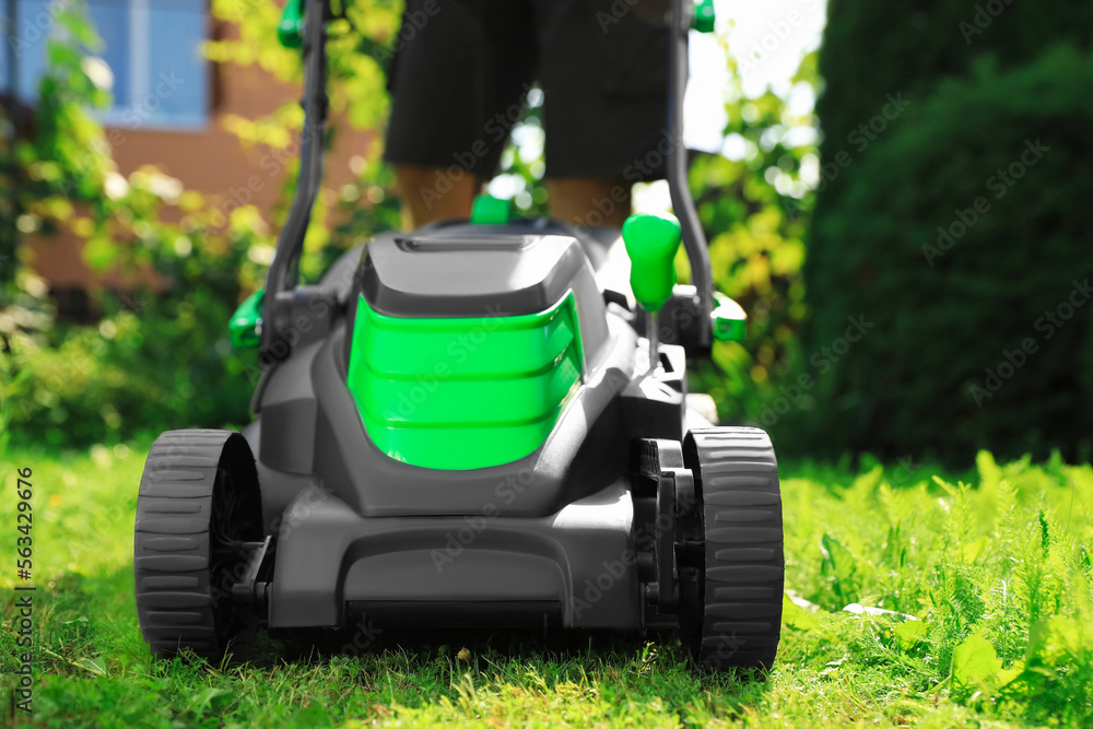 Fototapeta premium Man cutting grass with lawn mower in garden on sunny day, closeup