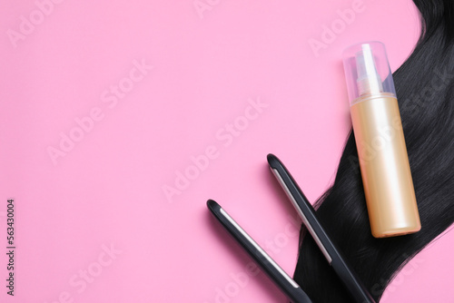 Spray bottle with thermal protection, iron and lock of black hair on pink background, flat lay. Space for text