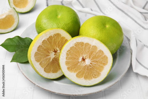 Whole and cut sweetie fruits with green leaves on white tiled table photo