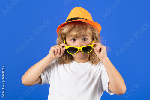 Fashion portrait of amazed kid in summer hat, t-shirt and sunglasses on blue studio isolated background.