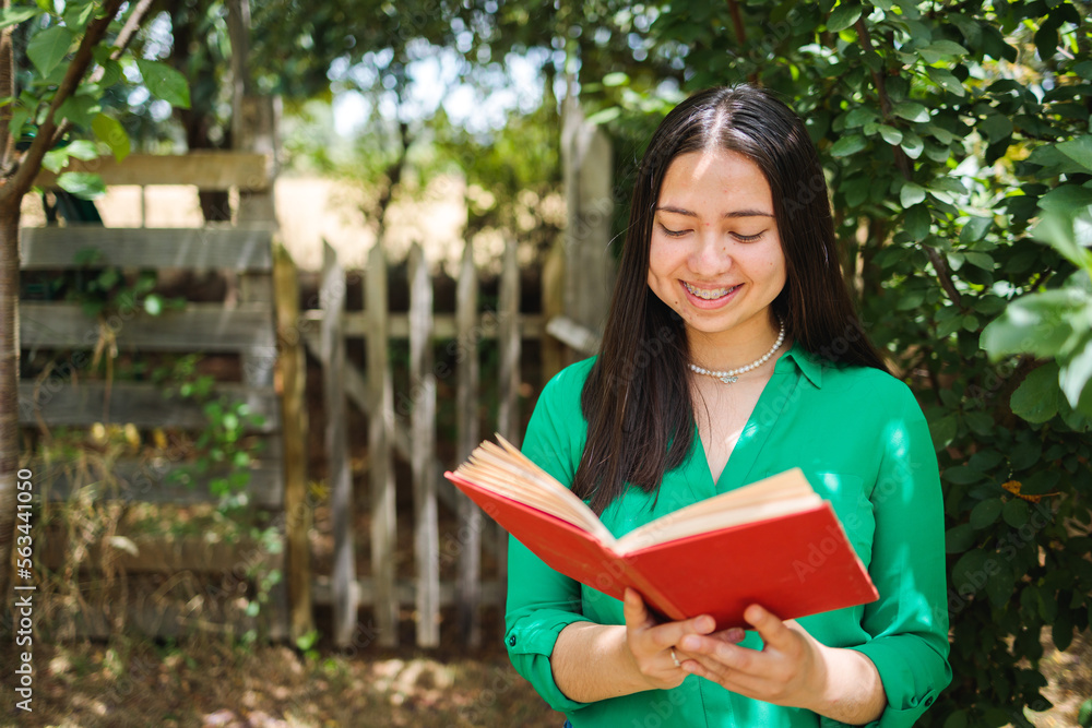 Obraz premium Smiling young farmer woman reading book in the field. Vertical shot. World book day. Copy space