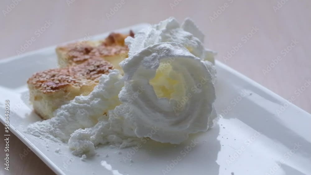 A piece of delicious cheesecake with whipped cream on a light wooden table Beautiful tasty white cake with white cream on cake stand cheesecake with caramel sauce whipped cream