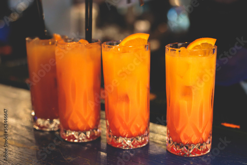 View of alcohol on a party, row line of orange red colored aperitif alcohol cocktails on a party, tequila sunrise, mimosa, spritz, screwdriver, margarita and others on a bar counter with bartender