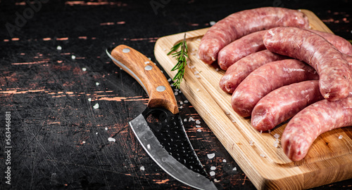 Cuadro en lienzo Raw sausages on a cutting board with a knife and rosemary.