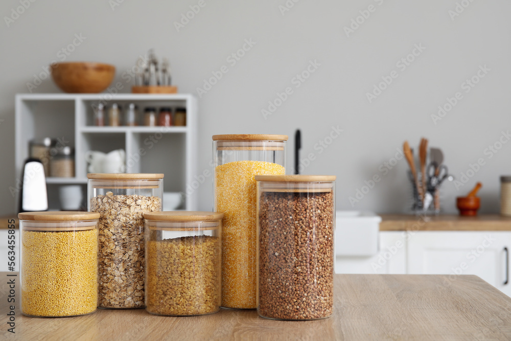 Glass jars with different cereals on wooden table in kitchen Glass jars with different cereals on wooden table in kitchen