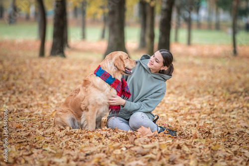 Young beautiful dark-haired girl in jeans plays in the spring park with a golden retriever.