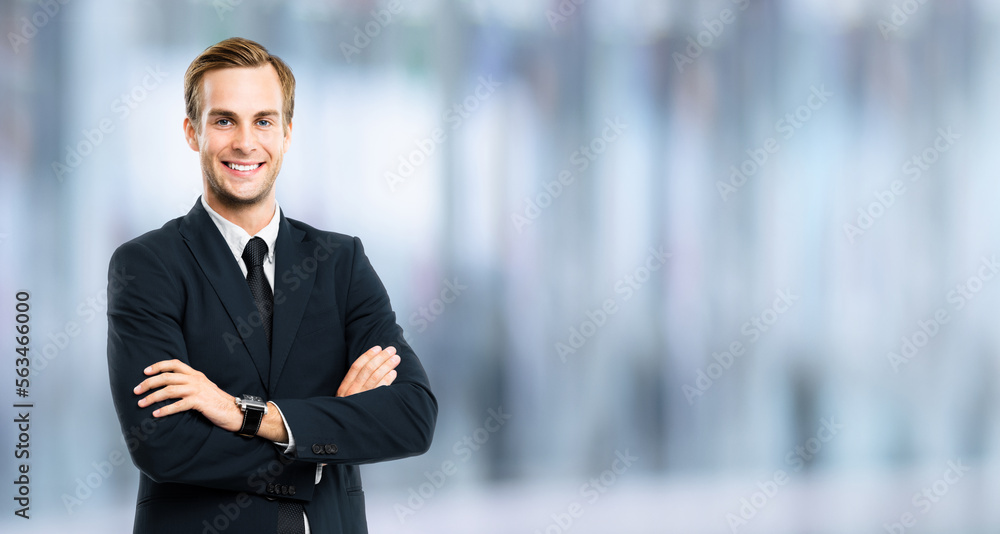Portrait of businessman in black suit, with folded arms, over blurred interior background. Smiling business man at studio picture. Copy space for text. Portrait of businessman in black suit, with folded arms, over blurred interior background. Smiling business man at studio picture. Copy space for text.