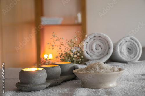 Bowl of sea salt and burning candles on couch in spa salon, closeup