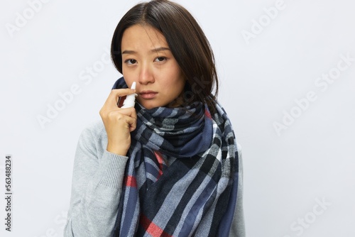 Asian woman flu cold with stuffy nose holds nasal spray and sprays nasal spray for allergies and covid 19 virus with sore throat on white background