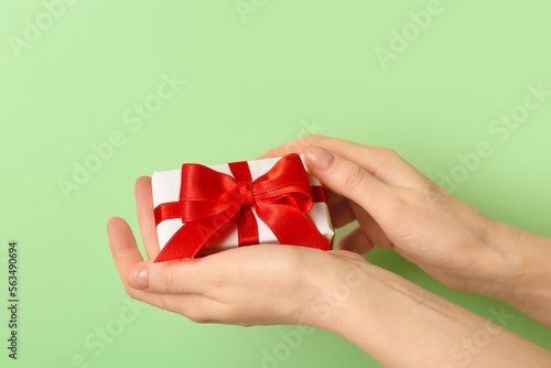 Woman holding gift box with beautiful bow on green background. Valentine's Day celebration
