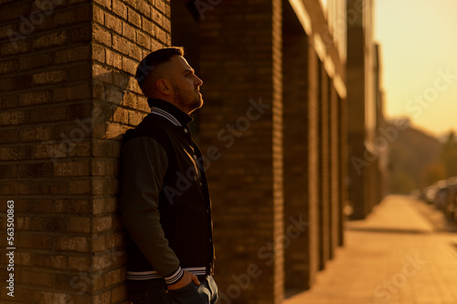 Fotografie Caucasian bearded man in a bomber jacket leaned against a brick wall