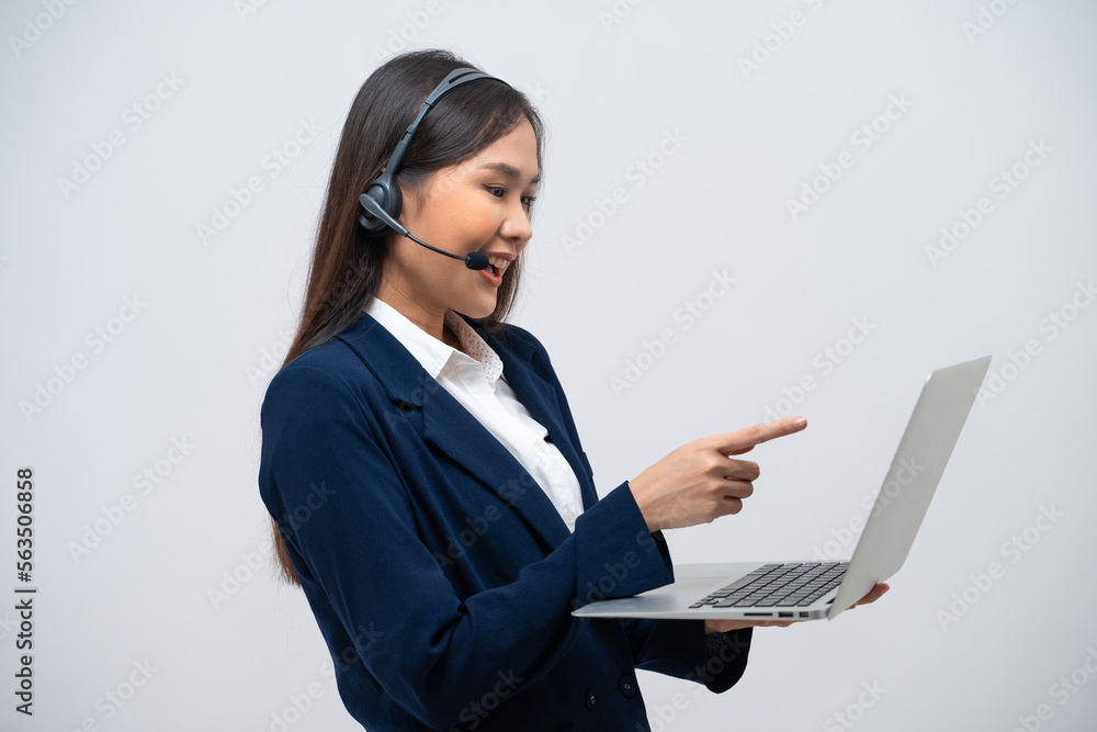 Beautiful Asian call center operator talking with customer using laptop isolated on grey background. Beautiful Asian call center operator talking with customer using laptop isolated on grey background.