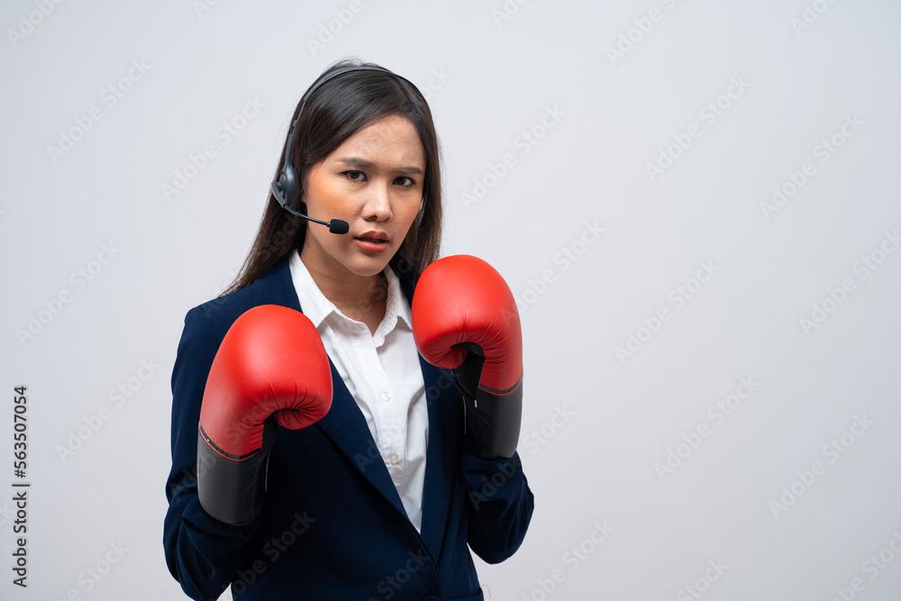 Beautiful Asian call center operator talking with customer using headset and microphone wearing boxing gloves isolated on grey background. Beautiful Asian call center operator talking with customer using headset and microphone wearing boxing gloves isolated on grey background.