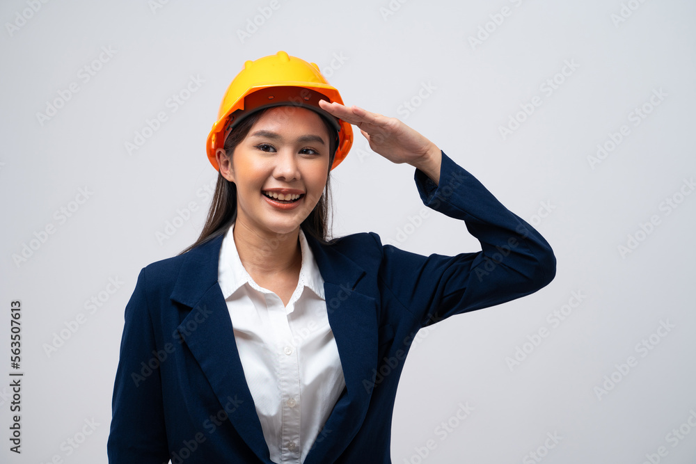 Portrait of Asian female engineer with hard hat making army salute isolated on grey background.
