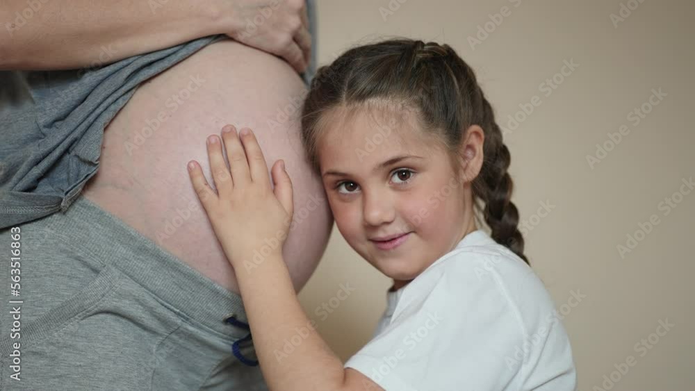 a little girl hugs her mother belly. happy family kid pregnancy newborn concept. the daughter dream sent her ear to the belly of the pregnant mother listens to the thrusts of the newborn brother a little girl hugs her mother belly. happy family kid pregnancy newborn concept. the daughter dream sent her ear to the belly of the pregnant mother listens to the thrusts of the newborn brother
