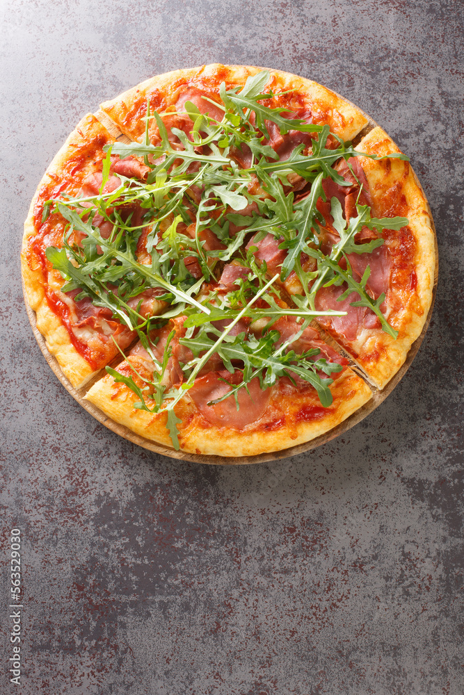 Pizza with prosciutto ham, cheese, tomato sauce and fresh arugula close-up on a wooden board on the table. Vertical top view from above Pizza with prosciutto ham, cheese, tomato sauce and fresh arugula close-up on a wooden board on the table. Vertical top view from above