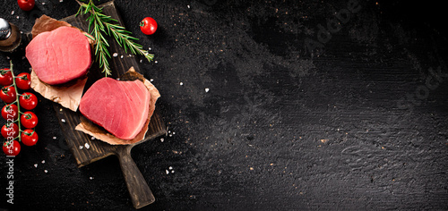 Raw tuna on a cutting board with tomatoes and rosemary. 
