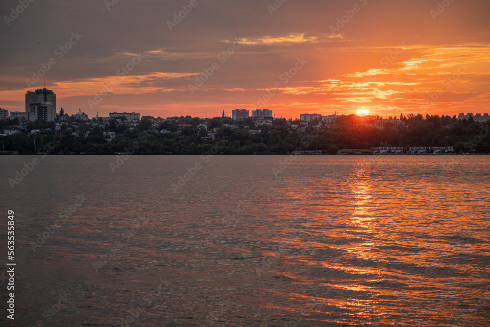 Orange sunset over river, town buildings silhouetted on horizon