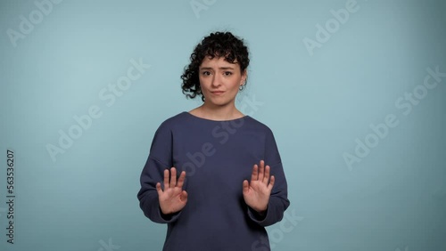 Portrait curly woman need distance showing no stop hands gesture looking at camera. Female wearing blue sweater express no way, no thanks or I don't need it sign on isolated light blue background