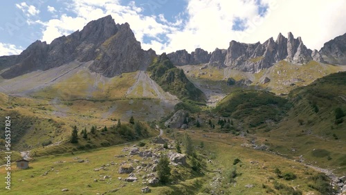 Rocky Mountains with clouds and green valley with trees reveal by aerial drone during summer in Tour du Mont Blanc, Alps, France