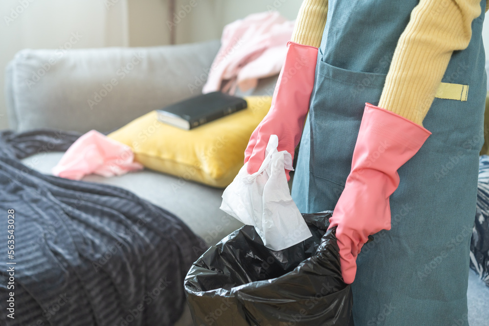 Tired household clean up, housekeeper asian young woman, girl hand holding tissue, napkin paper put in trash bin, cleaning in living room at home. Messy maid or housewife organizing dirty and untidy.