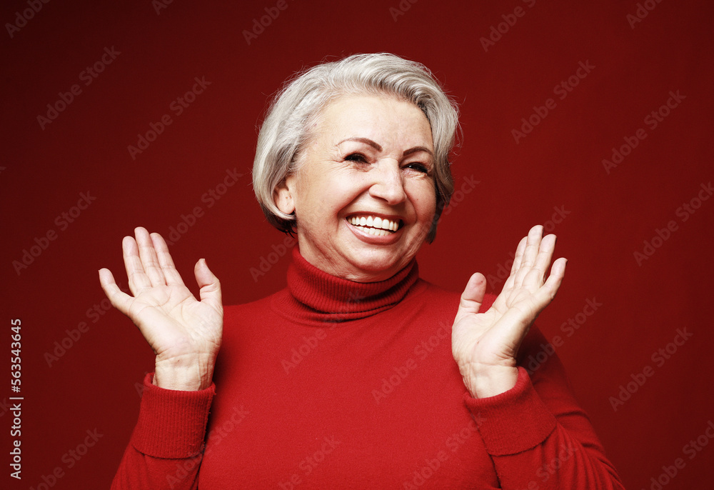 A cheerful old woman in a red sweater laughs and rejoices. Portrait on a red background. A cheerful old woman in a red sweater laughs and rejoices. Portrait on a red background.