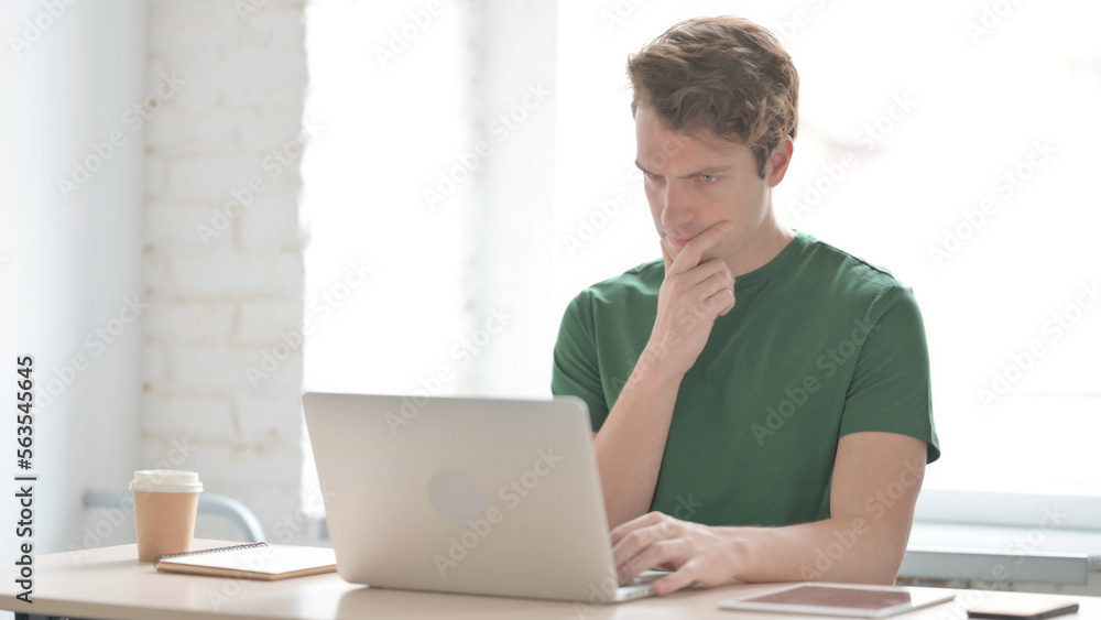 Young Man Thinking while Working on Laptop