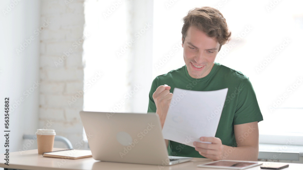 Young Man Cheering while Reading Business Report at Work Young Man Cheering while Reading Business Report at Work