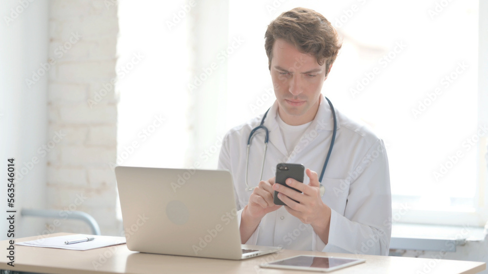 Young Doctor using Smartphone while using Laptop in Clinic Young Doctor using Smartphone while using Laptop in Clinic