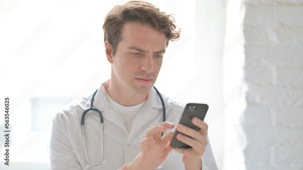Young Doctor using Smartphone While sitting in Clinic Young Doctor using Smartphone While sitting in Clinic
